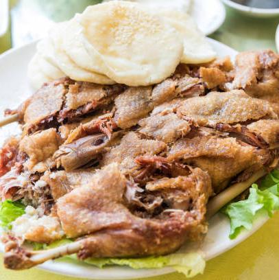 A plate of crispy duck, which has a golden-brown skin and is served with pancakes and green lettuce leaves.