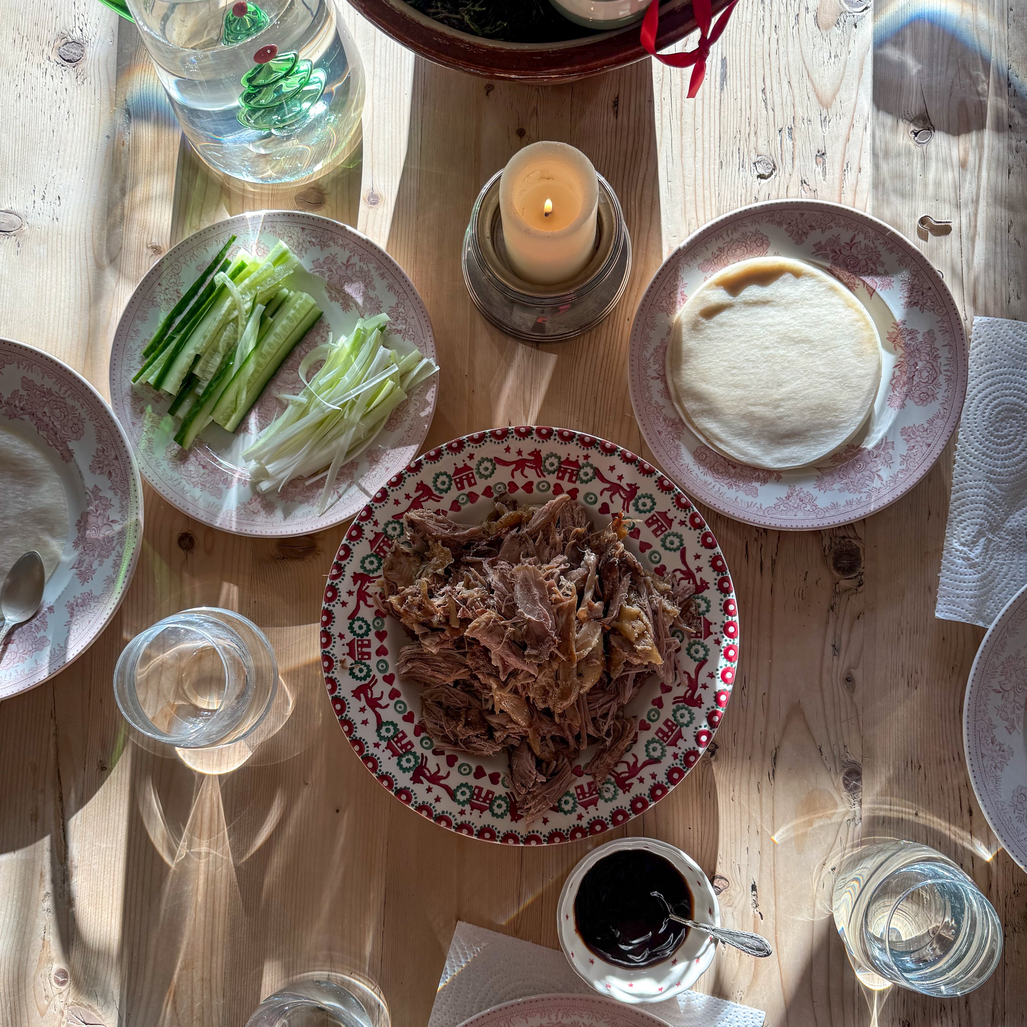 Dinner table with plates of crispy duck , glasses, and a candle on a wooden surface.